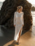 The Shea Long Sleeve T-Shirt Dress in White — model walking on the beach in the bamboo maxi dress with high side slit