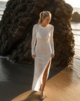 The Shea Long Sleeve T-Shirt Dress in White — model walking on the beach in the bamboo maxi dress with high side slit