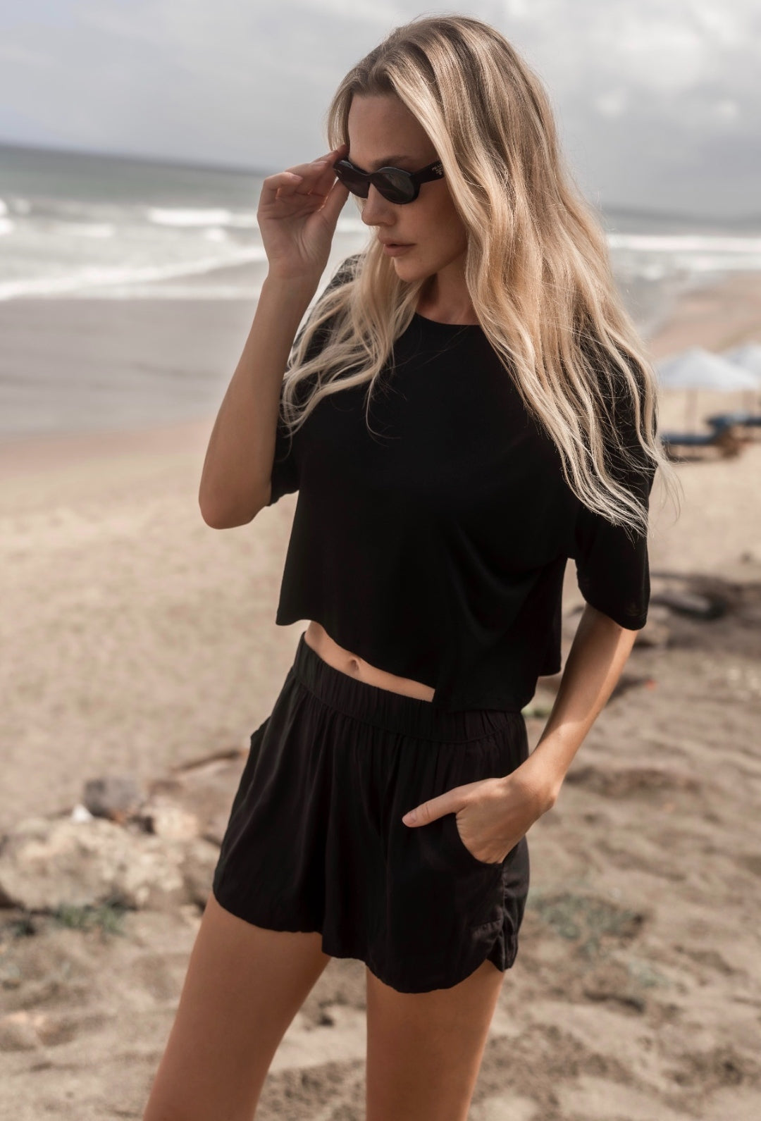 Model on the beach wearing The Travel T in black, boxy cropped fit