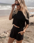 Model on the beach wearing The Travel T in black, boxy cropped fit